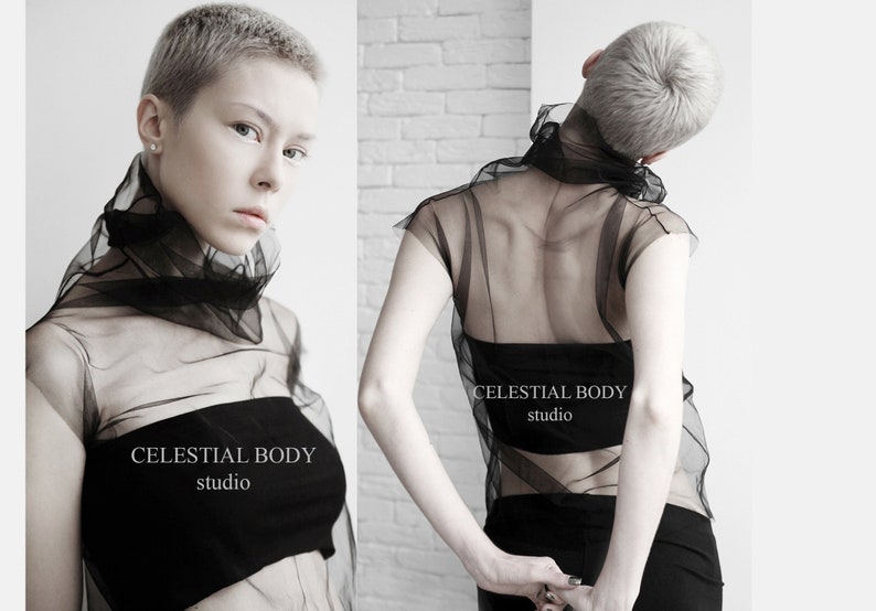 May include: A black sheer top with a high neck and short sleeves. The top is made of a lightweight, flowing fabric. The model is wearing the top with a black bandeau underneath. The text "CELESTIAL BODY studio" is printed on the front of the top.