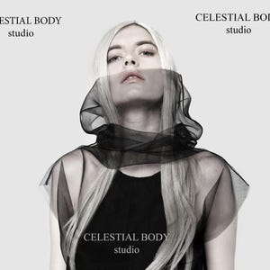 Puede incluir: Una mujer con el pelo largo y rubio lleva una capa negra transparente con capucha. El texto "CELESTIAL BODY studio" se repite tres veces en la imagen.