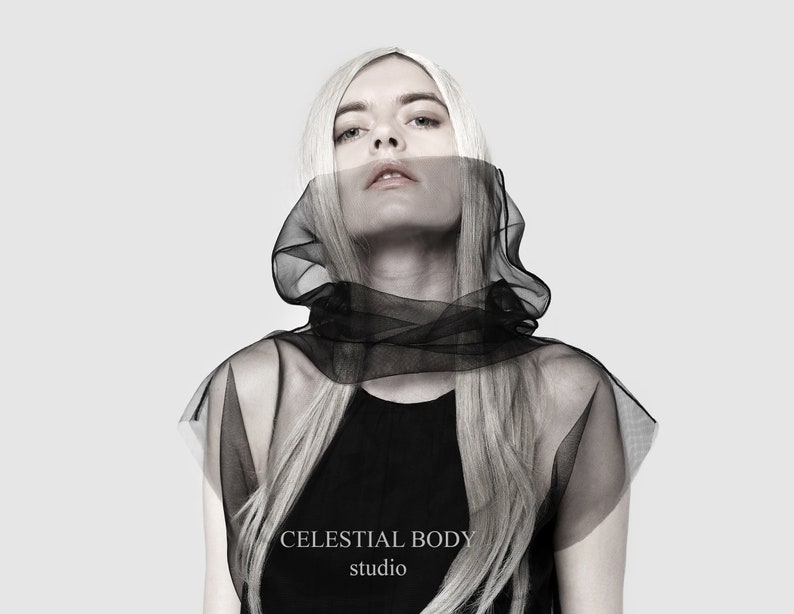 May include: A woman with long blonde hair wears a black sheer hooded top with the text "CELESTIAL BODY studio" on the bottom.
