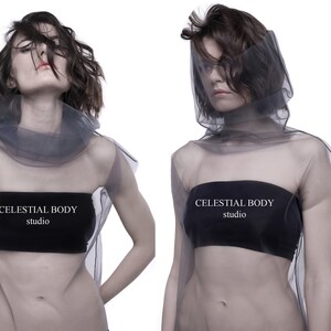 May include: Two models wearing sheer gray tops with black bandeau tops underneath. The tops have the text "CELESTIAL BODY studio" printed on them.