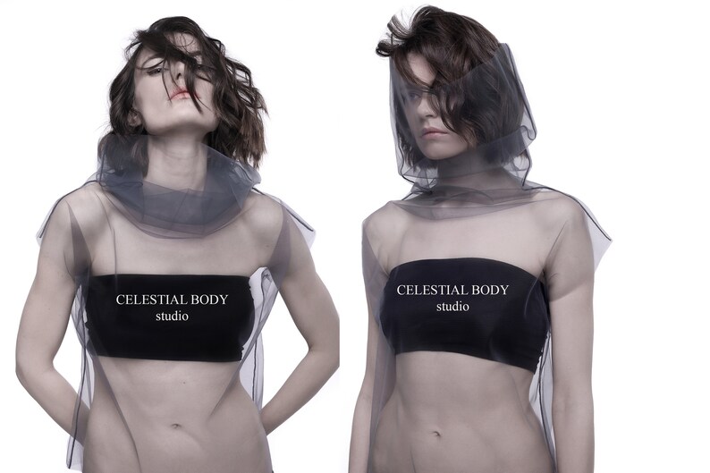May include: Two models wearing sheer gray tops with black bandeau tops underneath. The tops have the text "CELESTIAL BODY studio" printed on them.