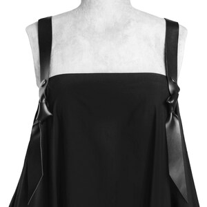Puede incluir: Un vestido negro sin mangas con escote cuadrado y dos tirantes de cinta negra que se atan en lazos en los hombros.