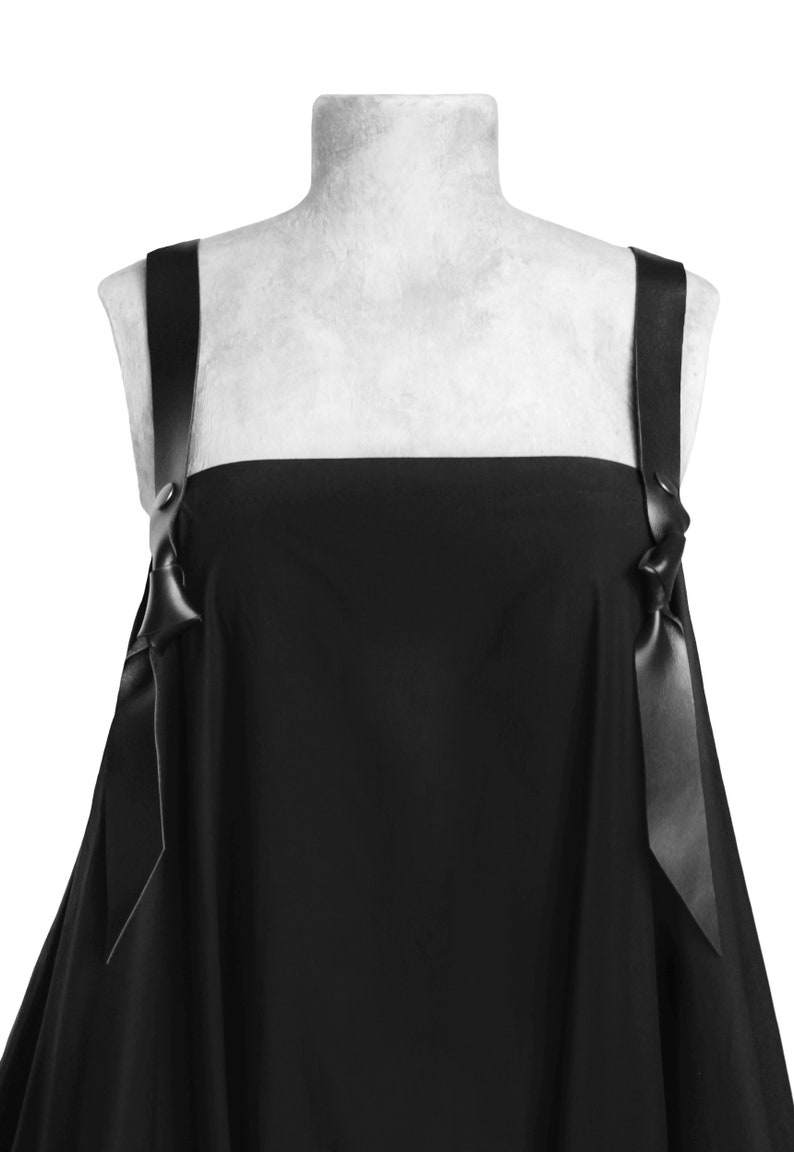 Puede incluir: Un vestido negro sin mangas con escote cuadrado y dos tirantes de cinta negra que se atan en lazos en los hombros.