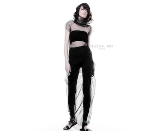 Puede incluir: Una mujer con un top negro transparente sobre un top negro de tirantes y pantalones negros. El top está fruncido en el cuello y tiene una falda larga y fluida. La mujer está de pie sobre un fondo blanco. "CELESTIAL BODY studio" está escrito en la esquina superior derecha de la imagen.
