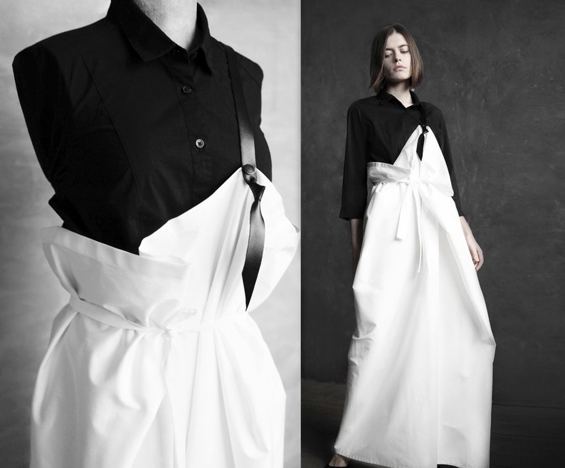 May include: A white, flowing, asymmetrical dress with a black ribbon detail. The dress is worn over a black button-down shirt.