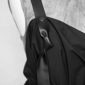 May include: A black sleeveless dress with a wide black leather strap that ties at the front. The strap has a metal button detail.