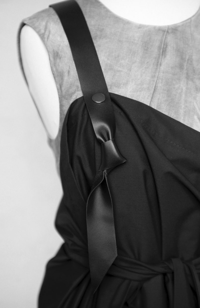 May include: A black sleeveless dress with a wide black leather strap that ties at the front. The strap has a metal button detail.