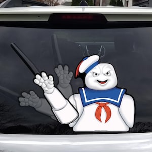 May include: A white vinyl decal of the Stay Puft Marshmallow Man from Ghostbusters, with a blue sailor collar, red neckerchief, and hat. The decal is applied to a car's rear window.