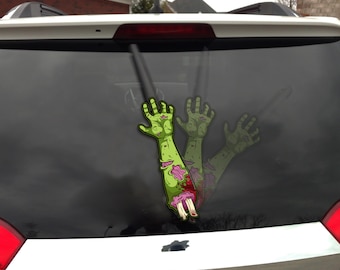 Op de afbeelding: Een groene zombie-armsticker met blootliggend bot en vlees, bloed en een gescheurde mouw. De sticker is aangebracht op de achterruit van een voertuig. De afbeelding toont een zombiethema.