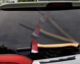 Op de afbeelding: Bijl met een rode kop en een houten steel, rustend op de achterruit van een voertuig. De bijlkop is rood met een zilveren blad. De steel is lichtbruin met tekst. De foto is buiten genomen.
