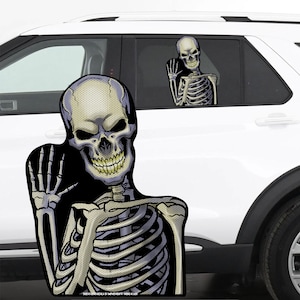 May include: A skeleton with a grinning skull waves from a car window. The skeleton is a sticker with a black and white grid pattern. The sticker is on a white car.