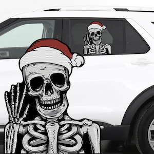 May include: A pair of car window decals featuring a skeleton wearing a Santa hat. The skeleton is waving with its hand. The decals are black, white, and red, and are placed on a white car.