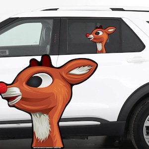 May include: A car window cling featuring a cartoon reindeer with a red nose, brown antlers, and white accents. The reindeer is smiling, with one cling on the car window and another on the car door.