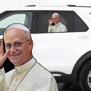 May include: A white car with a window sticker of a smiling man in a white robe and a white skullcap, waving. A large cutout of the same man is on the left side of the image.