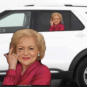 May include: A car window sticker featuring a woman with blonde hair wearing a pink shirt and making a funny face. The sticker is placed on the back window of a white car.