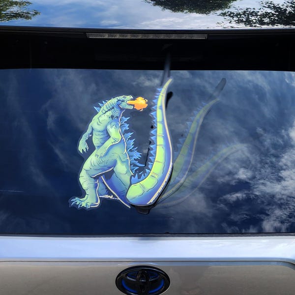 Kaiju Godzilla WiperTag decal waving tail attaches to rear vehicle wiper blades. Detachable, interchangeable, and weather resistant.