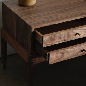 May include: A wooden nightstand with two drawers and brass knobs. The nightstand is made of walnut wood and has a dark brown finish.