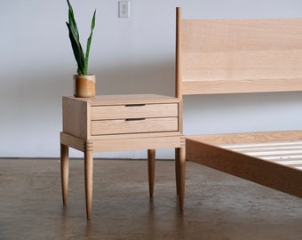 May include: A light wood nightstand with two drawers and tapered legs. The nightstand is next to a light wood bed frame with a headboard.
