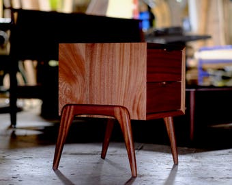 May include: A wooden nightstand with two drawers and four legs. The nightstand is made of a rich reddish-brown wood with a natural grain pattern.