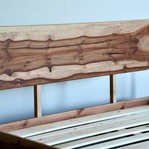May include: A wooden bed frame with a unique headboard made from a single piece of wood with natural wood grain patterns. The headboard is attached to the frame with metal brackets. The bed frame has a slatted base.