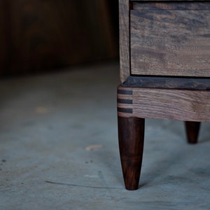 May include: A wooden dresser with a dark brown finish and a drawer. The dresser has four legs with a unique design and a dark brown finish.