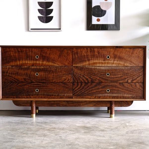May include: A six-drawer dresser made of dark wood with brass hardware. The dresser has a slightly curved base and sits on four brass legs.
