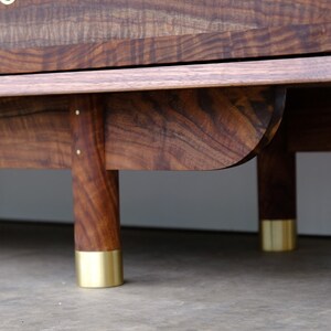 May include: A wooden cabinet with a dark brown finish and brass feet. The cabinet has a simple design with a flat top and a slightly curved bottom.