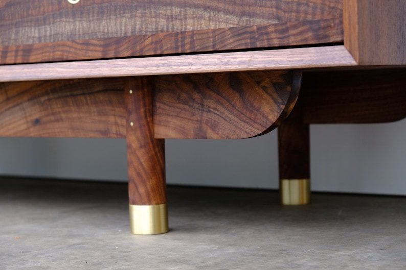 May include: A wooden cabinet with a dark brown finish and brass feet. The cabinet has a simple design with a flat top and a slightly curved bottom.