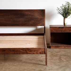May include: A dark wood bed frame with a slatted base and a matching nightstand with a drawer. The nightstand has a small vase with green foliage on top.