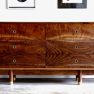 May include: A six-drawer dresser made of dark wood with brass hardware. The dresser has a curved base and sits on four brass legs.