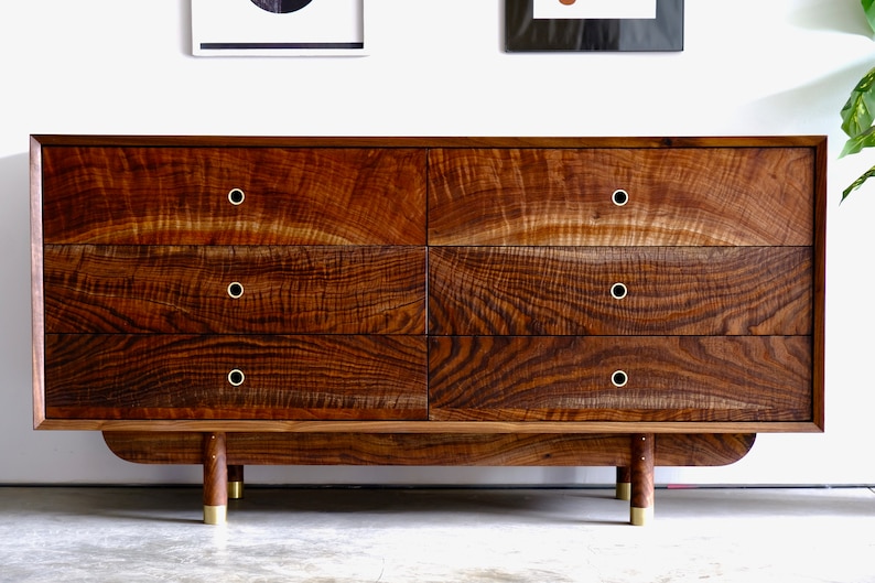 May include: A six-drawer dresser made of dark wood with brass hardware. The dresser has a curved base and sits on four brass legs.