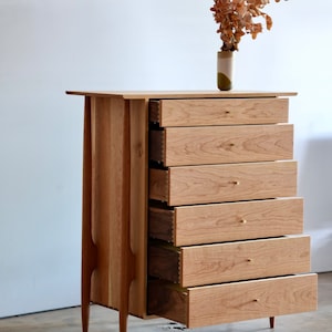 Op de afbeelding: Een dressoir met zes lades van licht hout met messing ladegrepen. De lades zijn open, waardoor de binnenkant van het dressoir zichtbaar is. Het dressoir staat op een betonnen vloer.