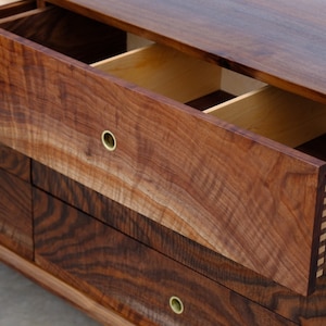 May include: A wooden dresser with five drawers, each with a brass knob. The top drawer is open, revealing a divided interior. The dresser is made of dark wood with a rich grain pattern.