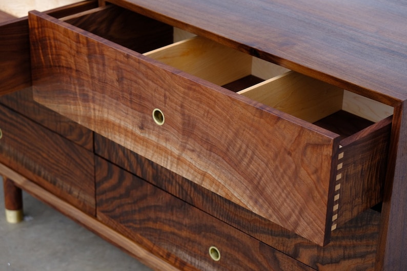 May include: A wooden dresser with five drawers, each with a brass knob. The top drawer is open, revealing a divided interior. The dresser is made of dark wood with a rich grain pattern.