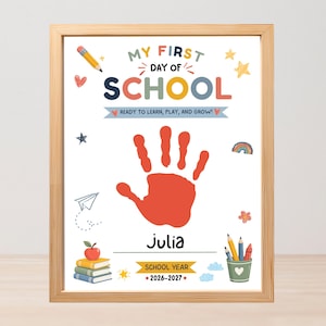Puede incluir: Una lámina enmarcada titulada My First Day of School con una huella de mano roja central, el nombre Julia y el año escolar 2026-2027. El diseño incluye ilustraciones de un lápiz, estrellas, avión de papel, arcoíris, manzana, libros y una taza.