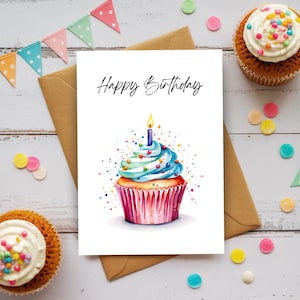May include: A white greeting card featuring the text Happy Birthday in black script above a watercolor illustration of a cupcake with blue frosting, colorful sprinkles, and a single lit candle in a pink pleated paper liner.