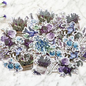 K&ouml;nnte beinhalten: Eine Sammlung von violetten und blauen Blumenaufklebern mit Lavendel, Rosen und Vergissmeinnicht. Die Aufkleber sind in einer Gruppe angeordnet und zeigen einen blauen Vogel.