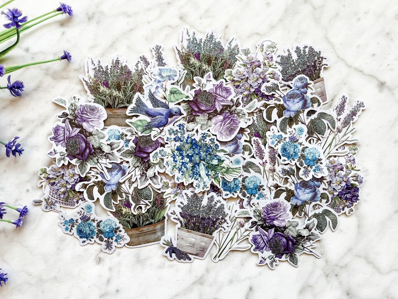 K&ouml;nnte beinhalten: Eine Sammlung von violetten und blauen Blumenaufklebern mit Lavendel, Rosen und Vergissmeinnicht. Die Aufkleber sind in einer Gruppe angeordnet und zeigen einen blauen Vogel.
