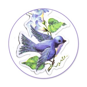 K&ouml;nnte beinhalten: Ein blauer Vogel mit Glitzerakzenten, der auf einer Rebe mit violetten Bl&uuml;ten sitzt. Der Vogel schaut nach rechts und hat seine Fl&uuml;gel ausgebreitet. Die Rebe hat gr&uuml;ne Bl&auml;tter und die Bl&uuml;ten sind wei&szlig; mit violetten Akzenten.