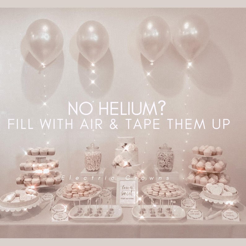 May include: A dessert table with white balloons, cupcakes, cookies, and a cake. The text "NO HELIUM? FILL WITH AIR & TAPE THEM UP" is displayed. The table is decorated with various sweets and treats for a party or event.