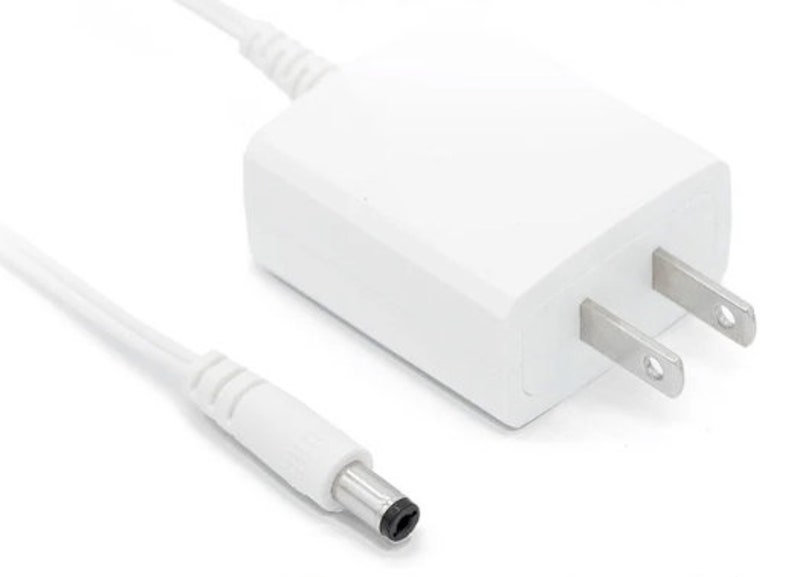 May include: White AC adapter with a US plug and a black barrel connector on the end of a white cord.