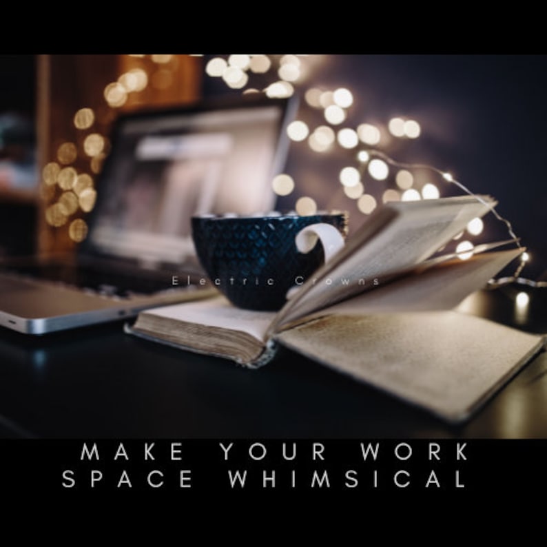 Op de afbeelding: Een donkerblauwe keramische mok met een wit handvat staat op een open boek, naast een laptop. De tekst "Electric Crowns" is zichtbaar op de mok. De woorden "MAKE YOUR WORK SPACE WHIMSICAL" staan onderaan de afbeelding.
