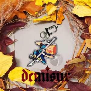 May include: A clear acrylic keychain featuring a cartoon character holding a sword and a block of cheese. The character is wearing a blue shirt, white gloves, and a pink hat. The keychain is attached to a silver metal ring.