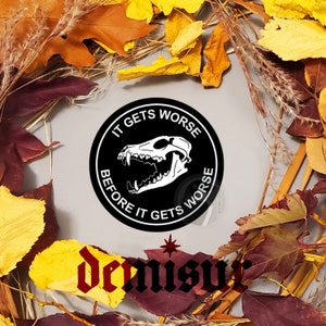 May include: A black and white circular sticker with the text "IT GETS WORSE BEFORE IT GETS WORSE" surrounding a white illustration of a skull. The sticker is surrounded by autumn leaves in shades of yellow, orange, and red.
