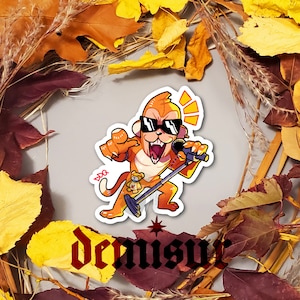 May include: A sticker featuring a cartoon monkey wearing sunglasses and holding a microphone. The monkey is orange and has a red bandana around its neck. The sticker is on a white background with the word "Dennis" written in black below it.