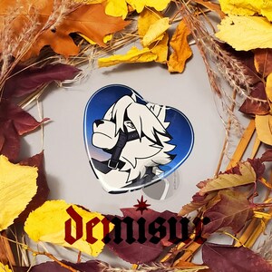 May include: A heart-shaped pin featuring a white wolf with blue eyes and a black leather muzzle. The wolf is set against a blue and purple gradient background.