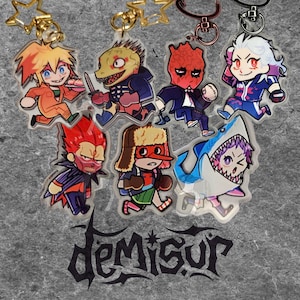 May include: A collection of acrylic keychains featuring colorful anime-style characters. Each keychain has a unique design, including a shark, a dinosaur, and other figures. The keychains are attached to gold and silver-colored metal rings.