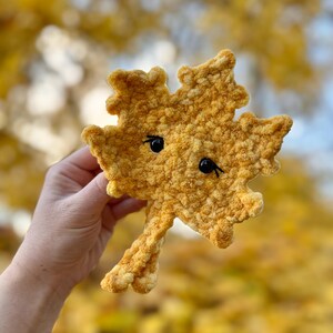 May include: A crocheted yellow leaf with a cute face. The leaf is made with a fuzzy yarn and has black eyes.