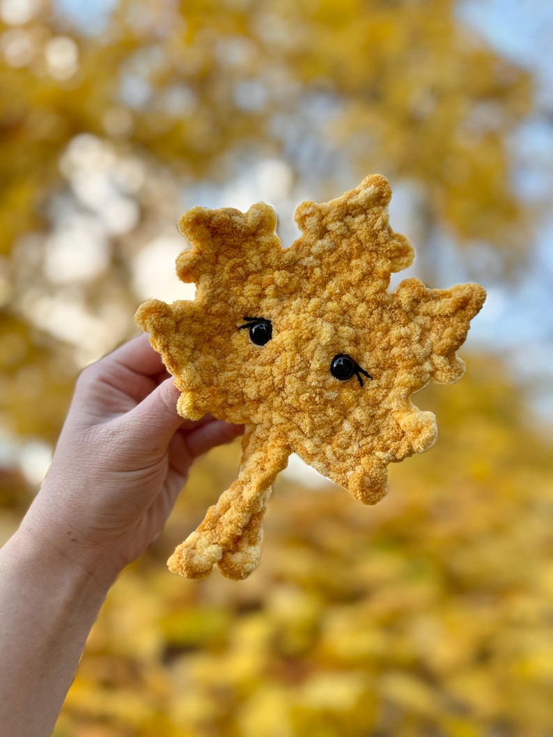 May include: A crocheted yellow leaf with a cute face. The leaf is made with a fuzzy yarn and has black eyes.