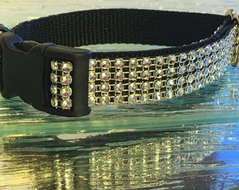 Puede incluir: Un collar de perro negro con ribete de diamantes de imitación plateados. El collar tiene una hebilla de plástico negro.